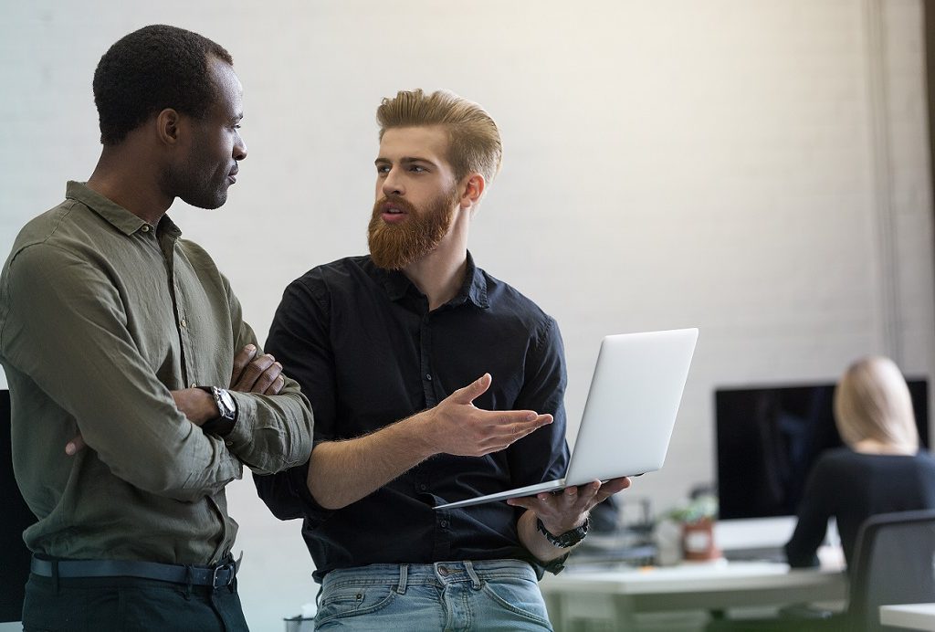 Two young smart business men discussing new project while standing in an office with laptop