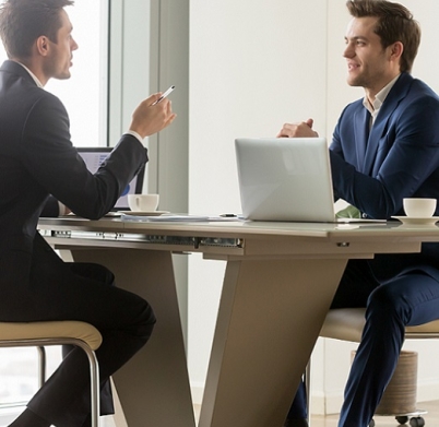 Two handsome businessmen sitting in comfortable chairs at desk with laptops in meeting room. CEO making important negotiation about companies partnership or corporate merger. Financiers planning deal